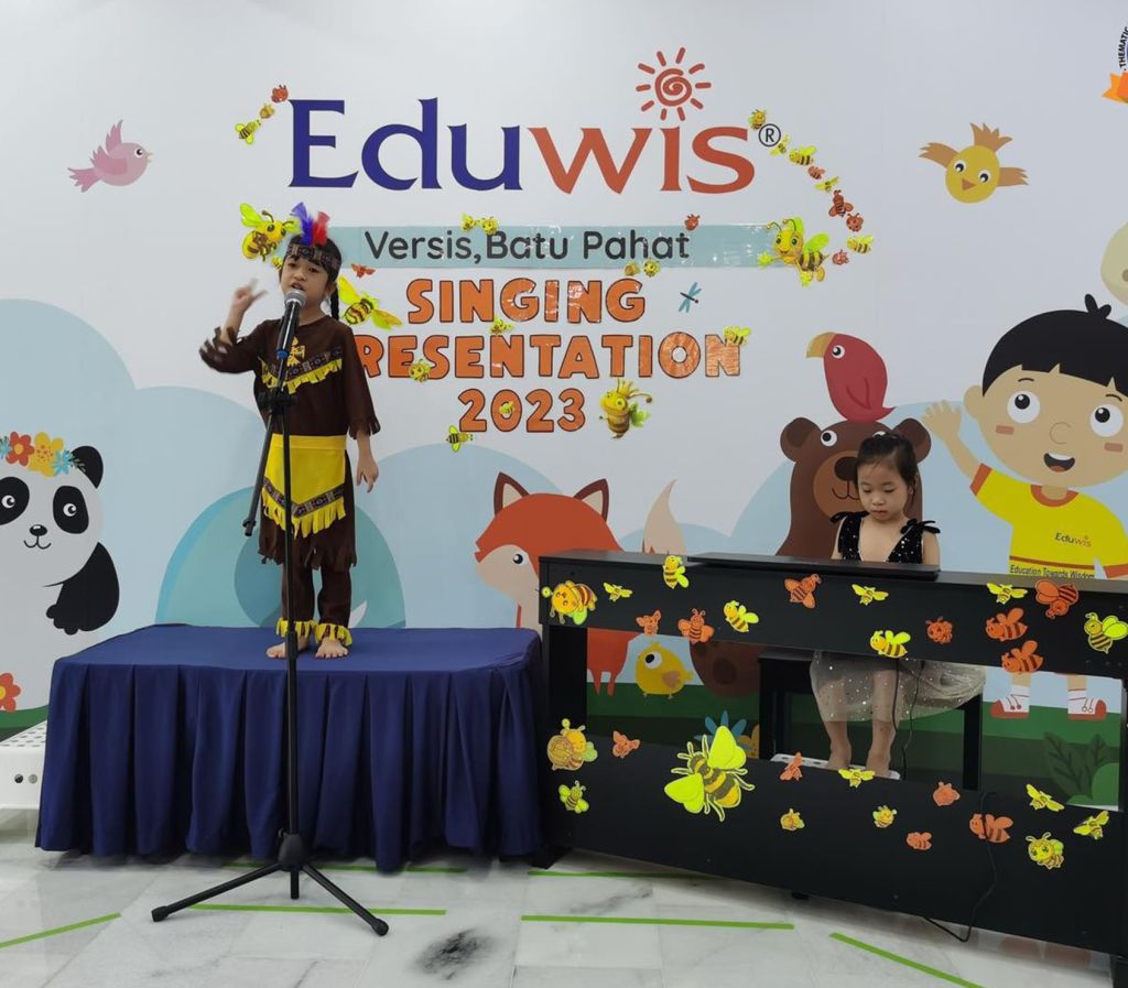 Children performing on stage for Eduwis’ Singing Presentation 2023 & Two little girls performing on stage during a singing presentation.