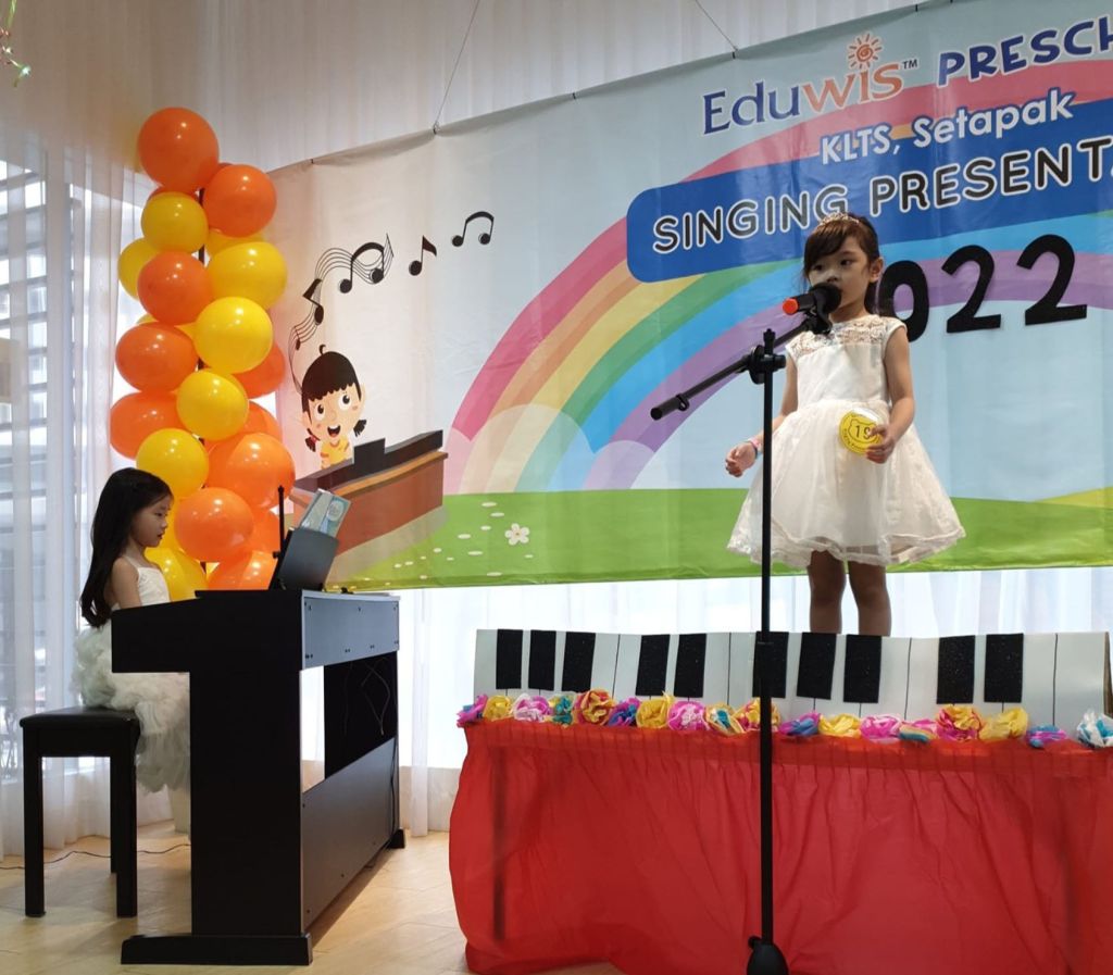 Children performing on stage for Eduwis’ Singing Presentation 2023 & Two little girls performing on stage during a singing presentation.