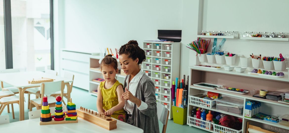 Adorable little girl and her teacher playing with some toys at kindergarten