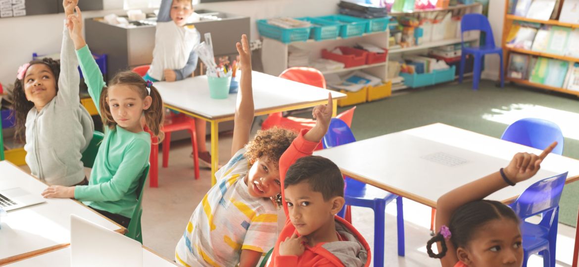 Overhead view of school kids raising hand to answer of teacher question in classroom at school