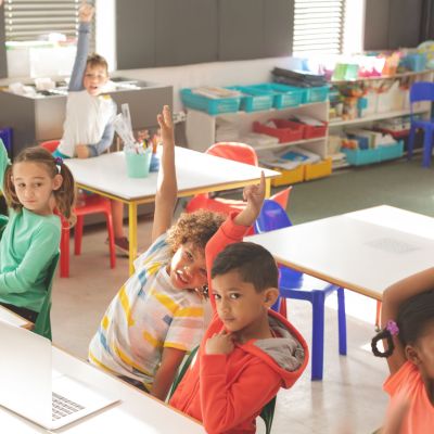 Overhead view of school kids raising hand to answer of teacher question in classroom at school